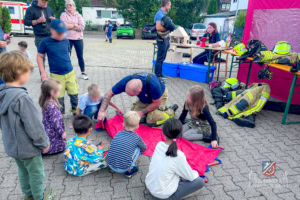 Ein Feuerwehrmann erklärt Kindern die Ausrüstung von Feuerwehrleuten